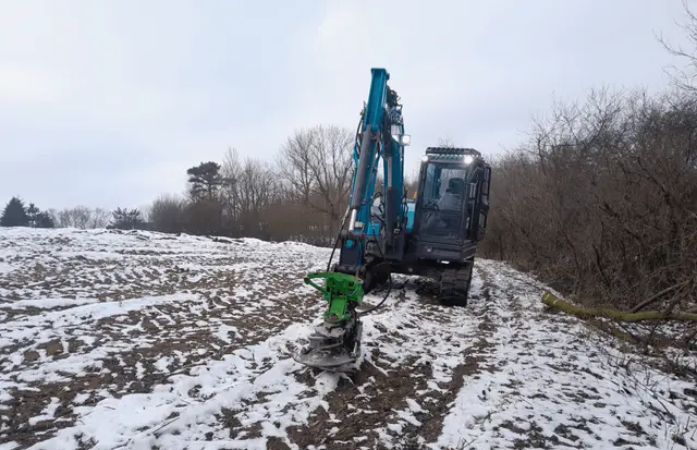 Kettenbagger mit Anbaufräse beim Freiräumen einer Fläche im Winter